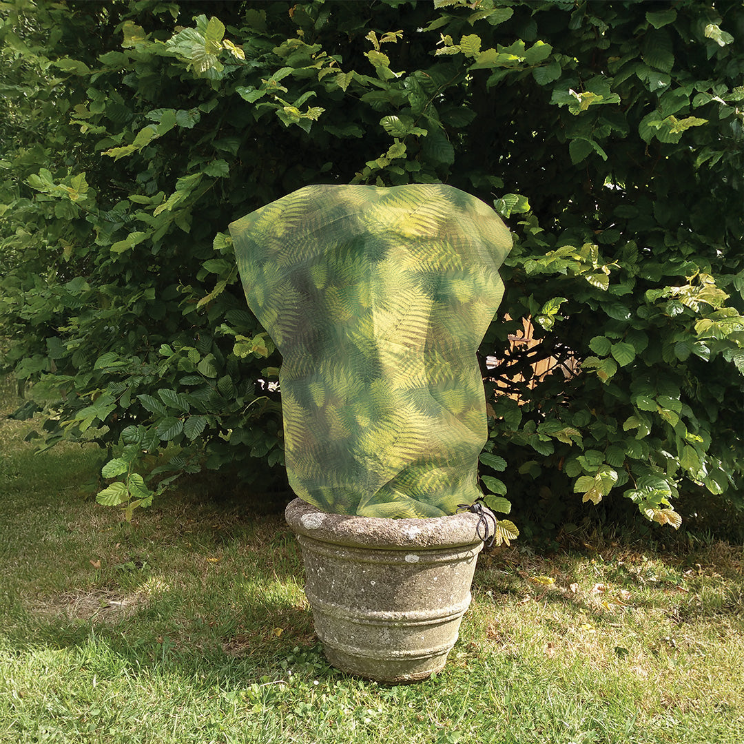 Green Fern Fleece Jacket winter plant protection on a plant in a stone urn in a garden setting